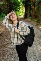 A woman carrying a backpack is standing on a path in the woods photo