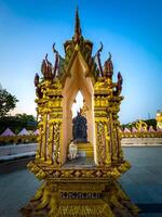 This eye-level, wide-angle shot captures an exquisitely ornate golden shrine, possibly a spirit house or small temple, with intricate detailing and vibrant colors under a clear twilight sky. A white photo