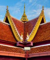 Captured from a low-angle perspective, this shot highlights the striking symmetry and vibrant colors of a traditional Thai temple roof. The rich, terracotta-colored tiles are beautifully complemented photo
