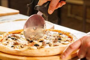 Cutting a freshly baked pizza with a pizza cutter photo