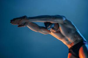Muscular swimmer in diving stance, arms forward, under dramatic lighting in studio setup. photo