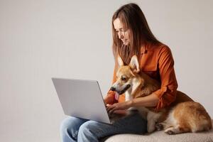 Woman working on laptop with Corgi dog on lap, cozy remote work lifestyle. photo