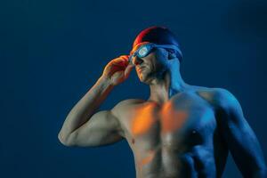 Focused swimmer in goggles and cap, lit by contrasting lights, ready to dive into action. photo