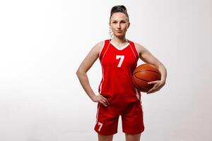 Confident female basketball player in red uniform posing with ball on white background, showing strength and determination in professional sports portrait. photo
