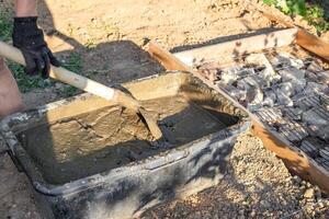 Man with gloves mixing cement in a black tub with a shovel to build a foundation photo