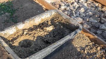 A black tub filled with a mixture of sand and water sits next to a construction site prepared with rocks and wire mesh for pouring concrete photo