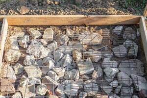 A construction site is prepared with rocks and wire mesh in a timber frame for pouring a concrete slab photo