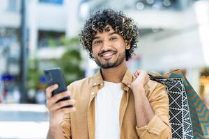 A smiling man holds his phone while carrying shopping bags, enjoying a day of shopping and using technology. photo