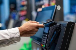 A person uses their smartphone to make a contactless payment at a point-of-sale terminal in a retail setting. The focus is on the hand and the device. photo