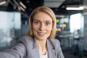 Successful woman looking into phone camera, talking to colleagues and partners using call and smartphone app. Working inside office of modern building. photo