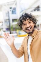 An attractive man waves hello in a call using his phone, smiling brightly photo