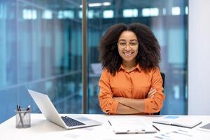 A smiling businesswoman with crossed arms sits in a modern office, radiating confidence and approachability. photo