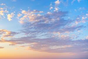 A panoramic photo of the sky with thin cirrus clouds illuminated by the setting sun in soft orange tones