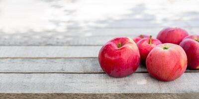 A bunch of bright red apples on a weathered wooden surface with soft lighting and enough space for text photo