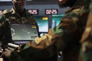 Military officers operating aerial systems on laptop device to support reconnaissance and target identification. Army specialists monitoring counterinsurgency operations with notebook software photo