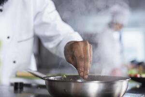 Black chef in modern kitchen adding herbs leaves to a dish on the stove, using fresh greenery and spices to elevate the flavors while cooking meal. Delicious culinary arts, gastronomy. photo