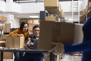 Workers team processing orders and retail shipments in small storehouse with taped boxes and labeled parcels. Local brand fulfillment supported by efficient logistics and delivery services. photo