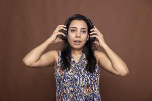 Portrait of female model wearing headphones, reacting to surprising audio content with an expressive face. Astonished woman with wide eyes and open mouth stares at camera, stunned by what she hears. photo