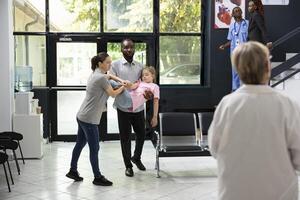 Diverse parents facing pediatric medical crisis after little girl collapses in lobby, asking for urgent support from black medical team in response to sudden panic and serious health scare. photo