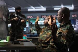 Dangerous terrorist threatening soldiers with rifles in command post. Insurgent using guns to control african american hostages during enemy base assault hijacking, during guerilla warfare armed conflict photo