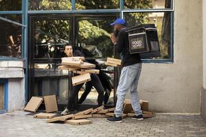 Delivery person dropping a huge pile of pizza boxes at the doorstep, client catching a few boxes and making a mess. Clumsy reckless courier destroying the fast food takeout order. photo