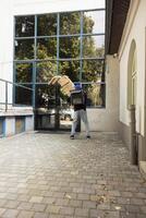 Clumsy pizza delivery man stumbles with massive stack of pizza boxes, dropping them at the customer doorstep. Shocked female client watches as the food order falls in a messy accident. photo