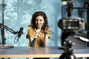 Enthusiastic internet show host hitting the record button on professional camera, using microphone to talk about today topic with subscribers. Media star filming creative vlog photo