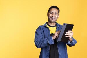 Male model smiling and accepting the payment on his mobile device, writing credit card numbers to purchase things online on websites. Young indian man processing the money transfer with the bank. photo