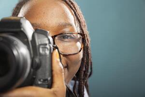Closeup of black female individual holding DSLR against blue background, showing camera handling techniques. African american professional photographer working in modern studio. photo