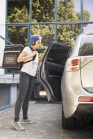 Takeaway employee getting out of the car with backpack to deliver food, delivering meal from a busy restaurant. Ensuring express food order takeout at the doorway, quick service. photo