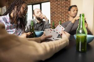 White woman holds playing cards, considering next move during friendly match with friends at home. Selective focus shows lady in action, chilling with diverse group, hanging out in cozy room. photo