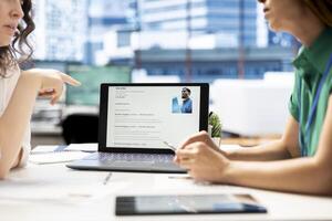 HR manager looking at CVs on tablet to vet selected applicants and ensure their skills match role needs. Headhunters in startup workspace reading resumes on device, assessing candidate work experience photo