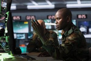 Military officer looking at surveillance monitor, analyzing data to allocate resources to units based on mission needs. African american agent examining strategic data on screen photo
