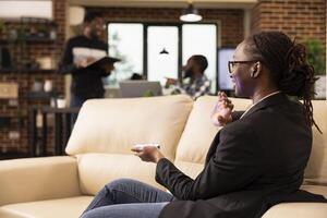 Black female entrepreneur using futuristic device to communicate with holographic interface and present data in tech forward workspace. African american team in background symbolizes startup synergy. photo