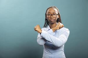 Confident african american woman poses in studio with her arms crossed in an X gesture. Black female individual looks directly at camera, expressing strength, rejection and bold determination. photo