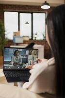 Confident female freelancer participates in online business meeting with investors on digital device. Multiethnic team engaged in conference, planning project ideas in brick wall apartment. photo