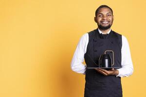 Restaurant worker serving people with tea before their dinner order, bringing the teapot at the table for professionalism. Waiter serves clients for satisfaction, service oriented industry. photo