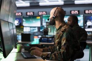 Military dispatcher in command post ready to respond to emergencies and communicate with soldiers on front lines. Middle Eastern war telecommunications operator in uniform talking in headset mic photo