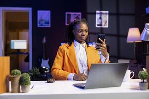 Young woman at home in living room typing messages on smartphone. Gen Z person holding mobile phone, enjoying relaxing leisure time talking with friends over online messaging app photo