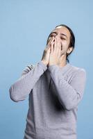 Middle eastern adult feeling joyful and amused with jokes in front of the camera, laughing and enjoying leisure activity in studio. Young person smiling and being positive against blue background. photo