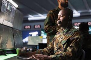 Counterintelligence agency dispatcher relays information from army intelligence analysts to front lines troops. African american radio communications operator in camouflage uniform talking in mic photo