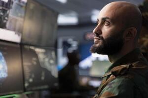 Army telecommunication systems agent using radio and satellite tech, providing combat support. Middle Eastern soldier managing communications networks, looking at monitors photo