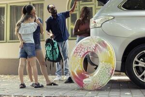 African American couple leaving on vacation with a friend and her child, preparing for a fun summer road trip. Diverse group packing the vehicle with luggage and beach essentials. Happy travel. photo