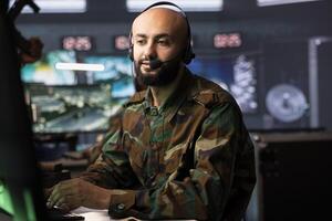 Agent in command room uses military tech to identify threats from enemies. Army operator in base of operations uses headset mic to communicate information to generals on war front line photo