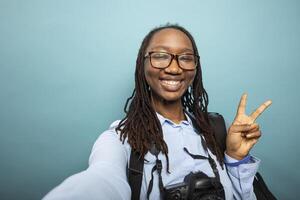 African american female vlogger giving peace sign to her online audience, recording herself in studio. Pov of excited black woman photographer making two finger, v gesture towards the camera. photo