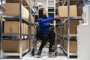 Asian woman with reduced mobility checking packages for custom orders, distribution hub focusing on retail operations for the small business. Accessible inclusive workspace with goods. photo