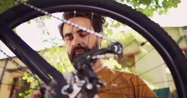 Close-up shot showing bicycle wheel being inspected and repaired by young dedicated caucasian man outdoor. Healthy active man examining bike tire for damages to fix with specialized tool in yard. photo