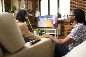 Diverse female friends playing console games, with television displaying game over message. African american and caucasian women sit relaxed, looking at TV screen, waiting to start new game. photo