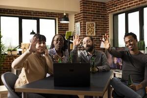 Male and female individuals waving towards device screen, participating in virtual call with long distance friends. African american and caucasian people making hello gestures during videoconference. photo