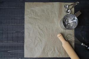 Baking utensils arranged on black wooden surface with parchment paper photo